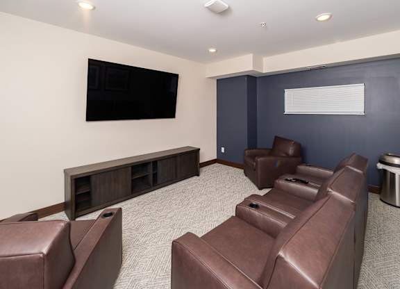 A room with brown leather chairs and a flat screen TV mounted on the wall.