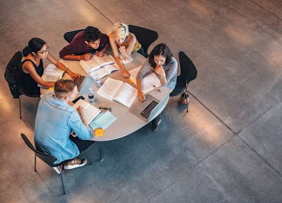 A group of people sitting around a table with laptops and papers.