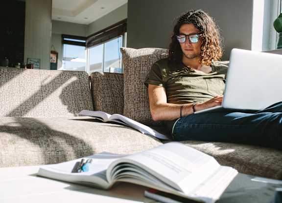 A person is sitting on a couch with a laptop and a book.