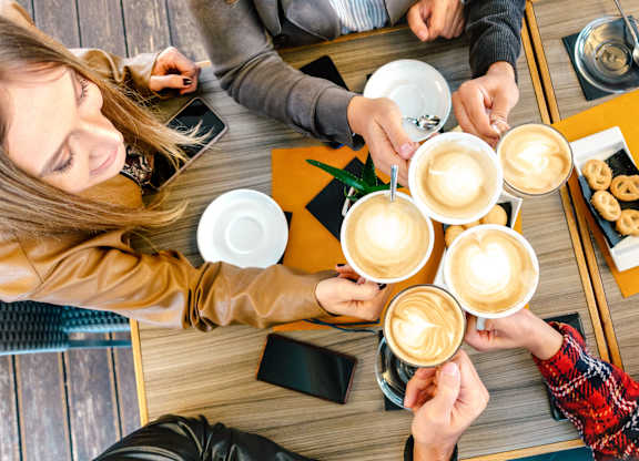 A group of people are gathered around a table, each holding a cup of coffee with a heart design on top.