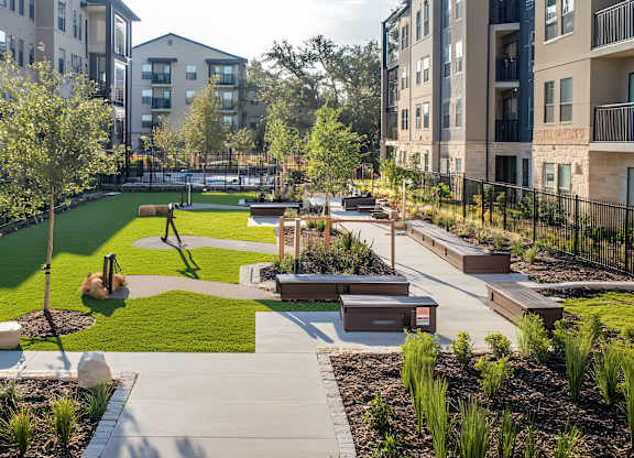 A park area with a walking path and benches is surrounded by apartment buildings.