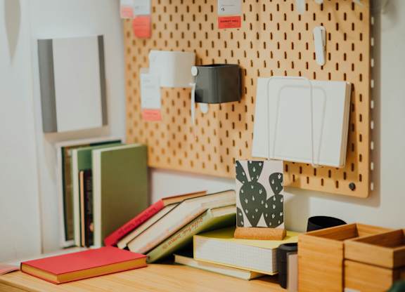 A pegboard with various items pinned to it and a desk with a red notebook and other items.