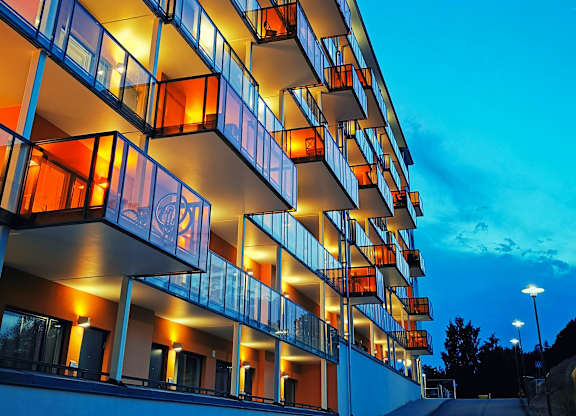 A modern building with balconies is illuminated by warm lighting.