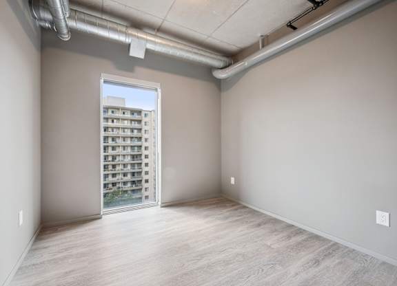 Empty bedroom with exposed ductwork and window at Ophelia on Queen Apartments, Kitchener, N2G 0E7