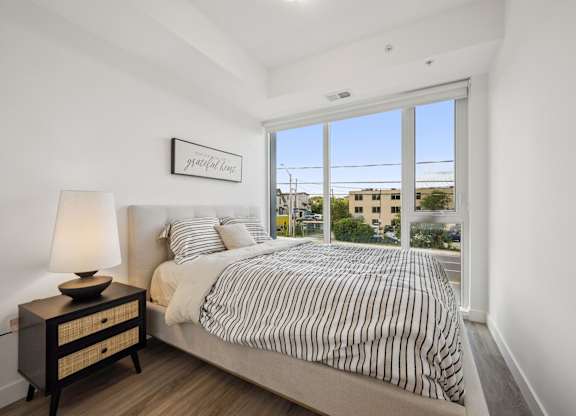 Bright bedroom with large windows and striped bedding at The Maverick Apartments, Kitchener, Ontario