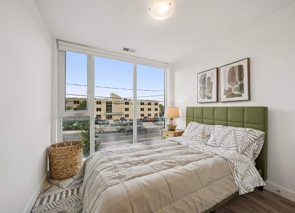 Bedroom with large windows and green upholstered headboard at The Maverick Apartments, Ontario, N2H 0E3