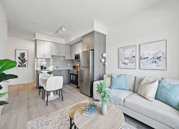 A modern living room with a grey sofa, a wooden coffee table, and a kitchen area in the background at Roxy Apartments, Hamilton, ON, L8H 0B7