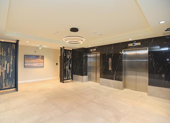 A spacious lobby with marble floors and a modern art piece on the wall at Roxy Apartments, Ontario