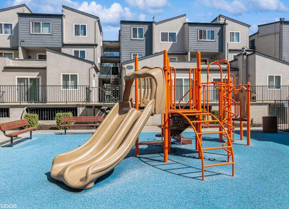 A playground with a slide and swings in front of apartment buildings.