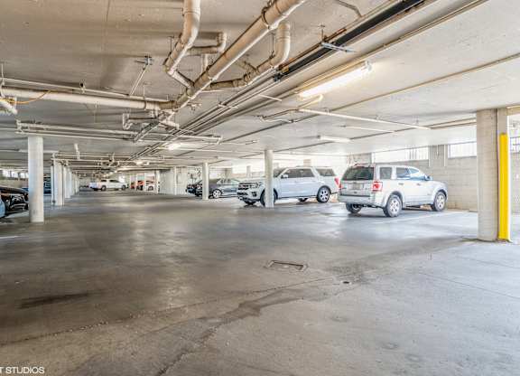 A parking garage with several cars parked and a yellow pole on the right side at Oak Center Apartments, California, 94607