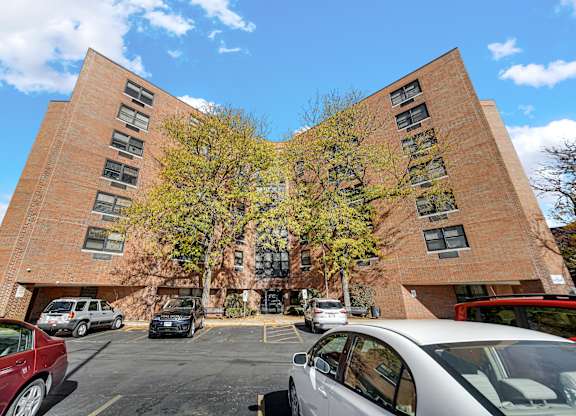 A parking lot with cars and a red car in the foreground at Fullerton Court Apartments, Chicago, Illinois
