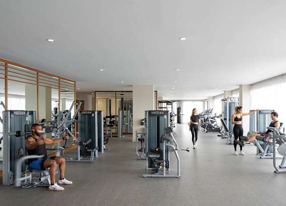A man is working out in a gym with a woman stretching in the background. at Palma, Doral, FL, 33166