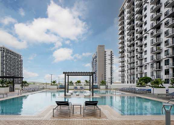 A pool area with a pergola and chairs in front of apartment buildings. at Palma, Doral, Florida