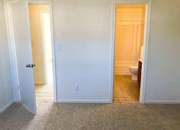 A bathroom with a toilet and a doorway leading to another room.