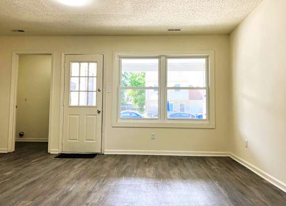 A room with a white door, a window, and a wooden floor.