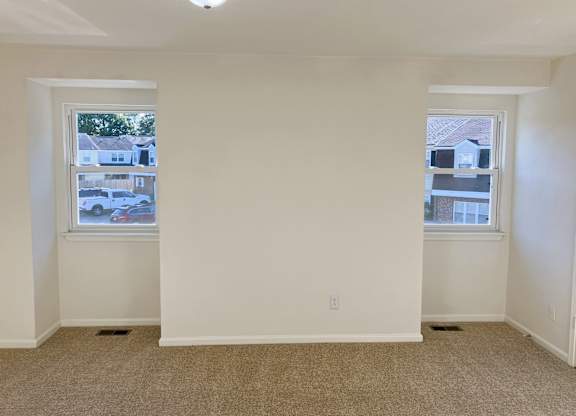 A room with two windows and carpeted floor.