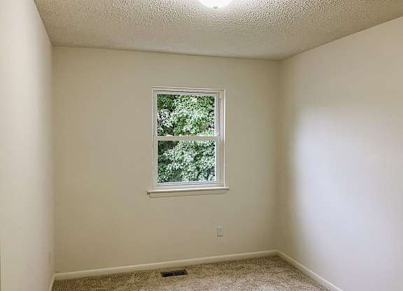 A room with a window and a carpeted floor.