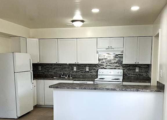 A kitchen with white cabinets and a black backsplash.