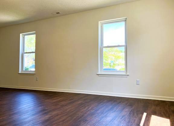 A room with two windows and wooden floors.