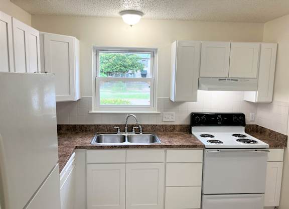A white kitchen with a refrigerator, stove, and sink.