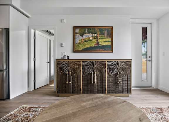 A painting of a landscape hangs above a wooden console in a white room.