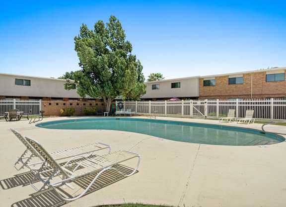 A pool with chairs and a tree in front of a building.