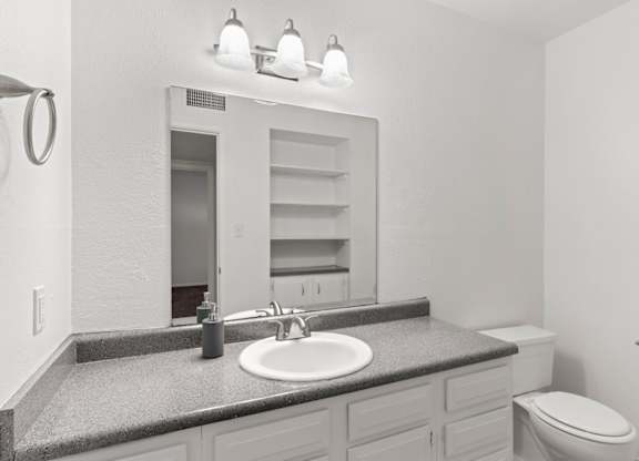 A bathroom with a sink, mirror, toilet and a towel ring on the wall.