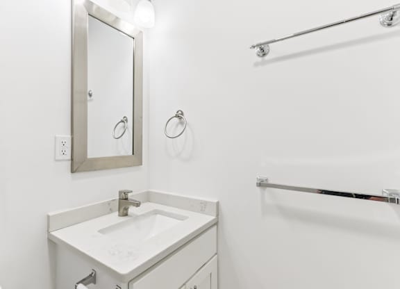A white bathroom with a sink, mirror, and towel rack.