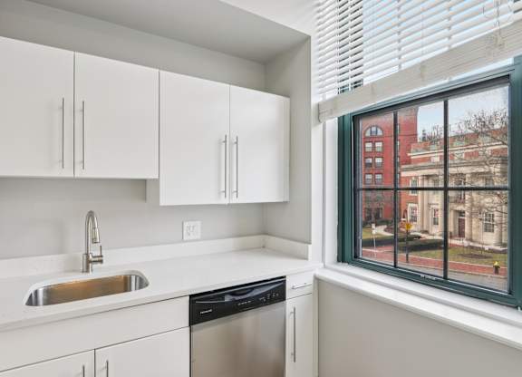 A kitchen with white cabinets and a window overlooking a city street.
