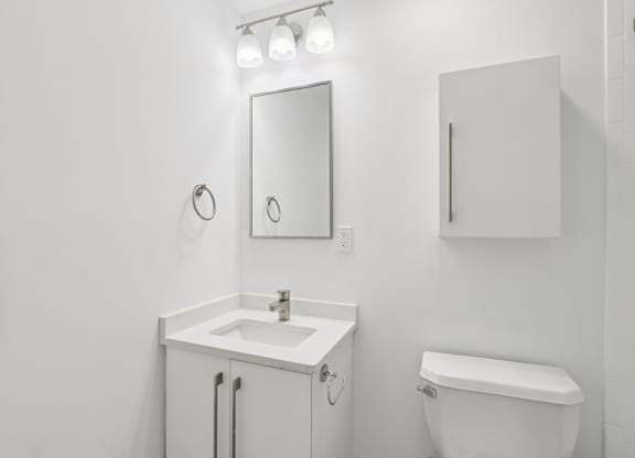 A white bathroom with a sink, mirror, and toilet.