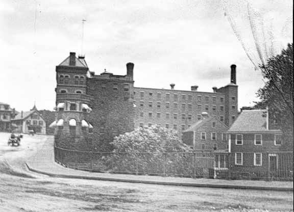 A black and white photo of a large building with a tower and a smaller building to the right.