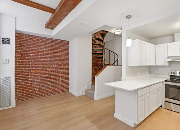 A kitchen with white cabinets and a brick wall.