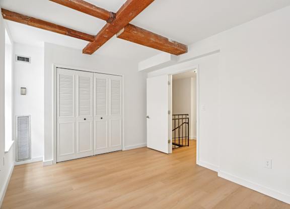 A room with white walls and wooden floors has a white door and a white wardrobe.