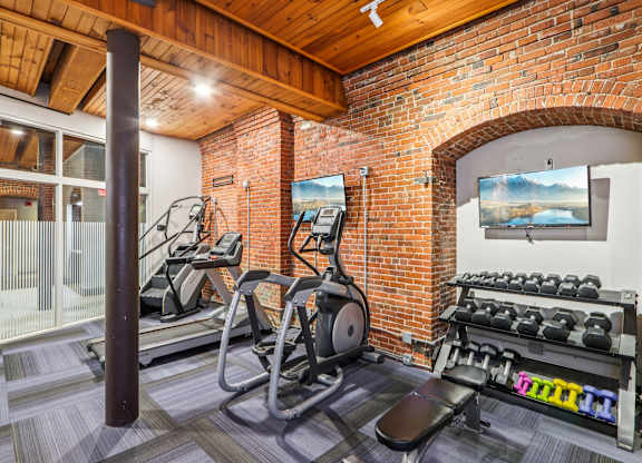 A gym with a brick wall and a row of treadmills.