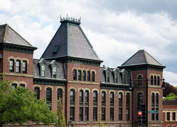 A large red brick building with a black roof and a green lawn in front.