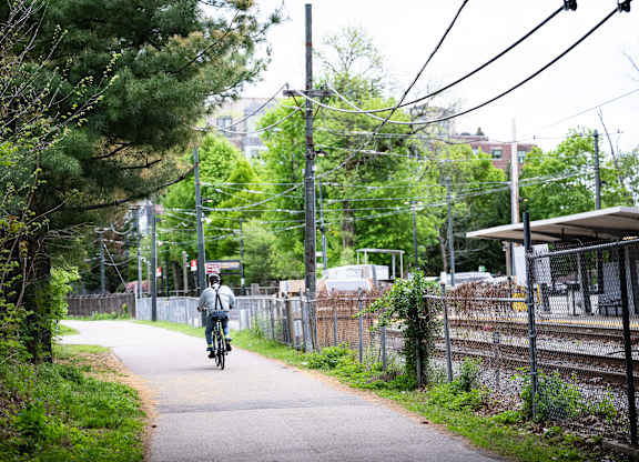 A person riding a bike on a paved path next to a fence.