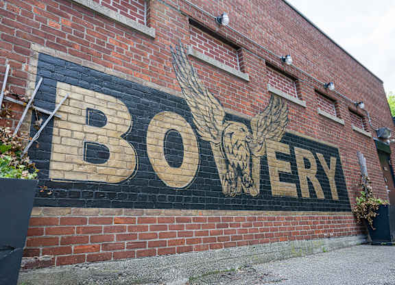 A brick wall with a mural of a bird and the word "BOWERY" painted on it.