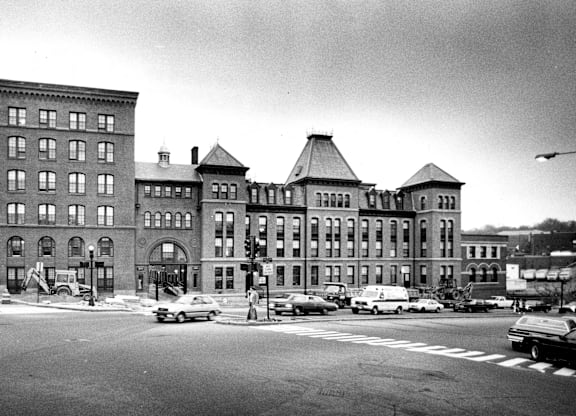 A black and white image of a street with cars and buildings.