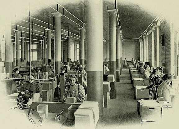 A black and white image of a large room with people sitting at desks.