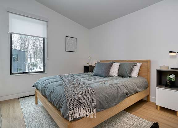 A bedroom with a bed, nightstand, and window at The Grove Apartments, Ontario