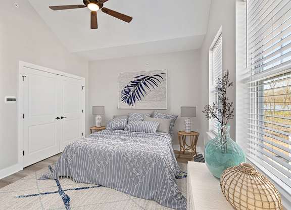 A bedroom with a bed, a ceiling fan, and a painting of a palm tree on the wall.