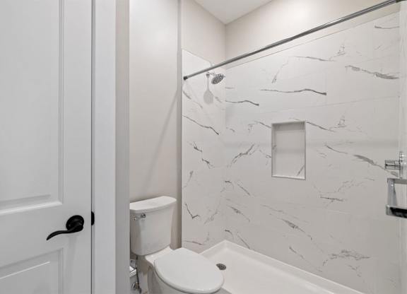 A white bathroom with a marble wall and a white toilet.