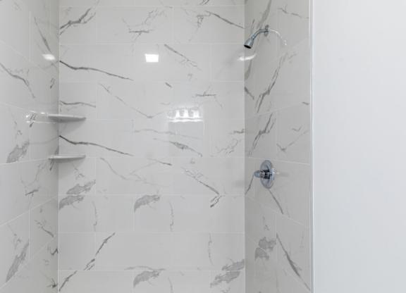 A white marble shower with a silver shower head and a silver barrier.