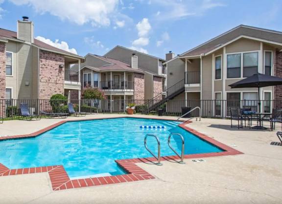A swimming pool surrounded by a brick wall and a patio area with chairs and umbrellas.