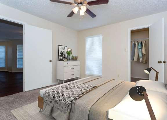 A bedroom with a bed, a couch, a ceiling fan, and a window with blinds.