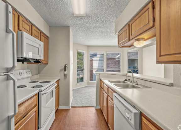 A kitchen with a white refrigerator, white oven, white microwave, white dishwasher, and wooden cabinets.
