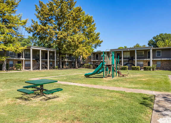 A playground with a green slide and picnic table.
