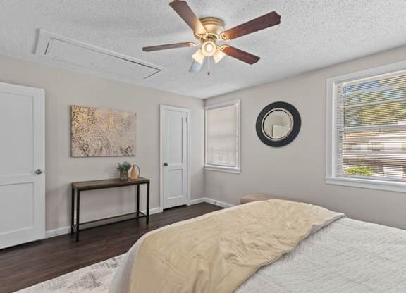 A bedroom with a bed, a table, a painting, a mirror, and a window.