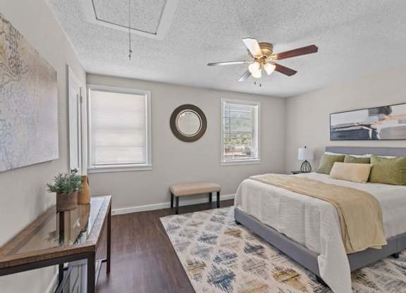 A bedroom with a bed, a bench, a table, and a ceiling fan.
