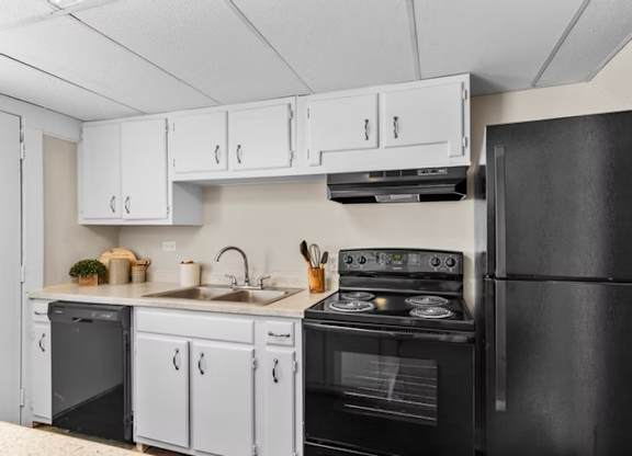 A black refrigerator is on the right side of a kitchen with white cabinets.